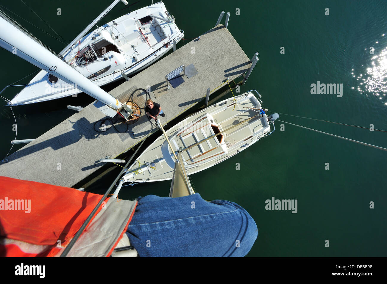 At the masthead. A sailor at the top of his mast for maintenance, photographs the yacht below. Stock Photo