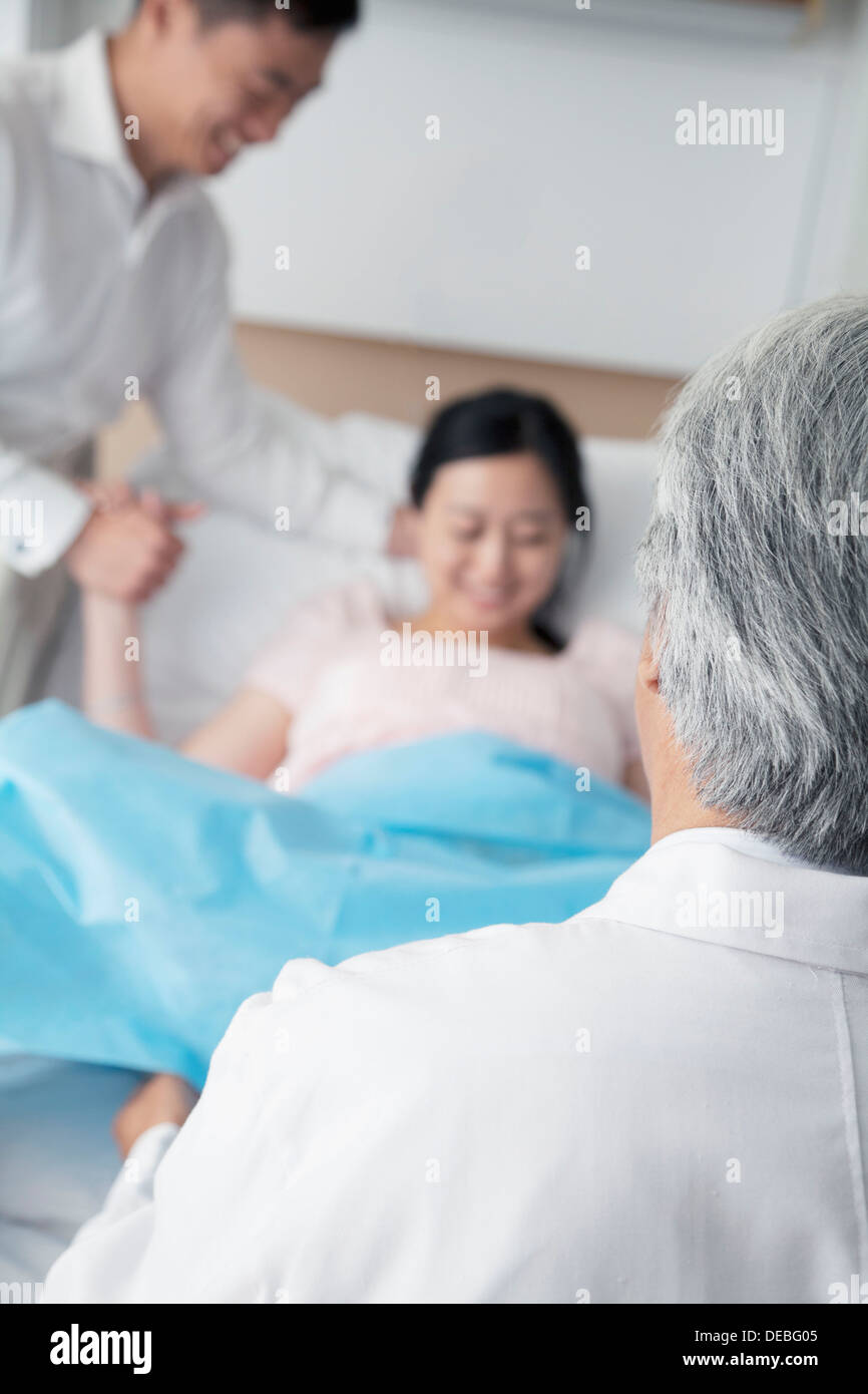 Women in labor holding her husbands hand with doctor in the foreground in the hospital Stock Photo
