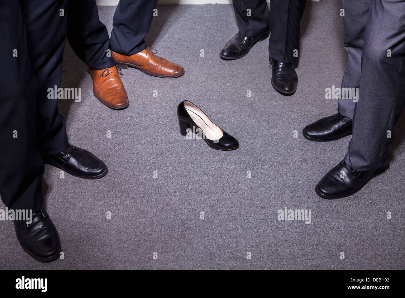 Businessmen standing in a circle around a woman's high heel, feet and legs only Stock Photo