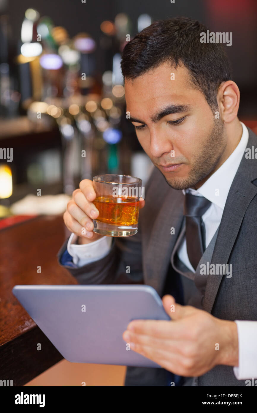 Serious businessman working on his tablet computer while having a whisky Stock Photo