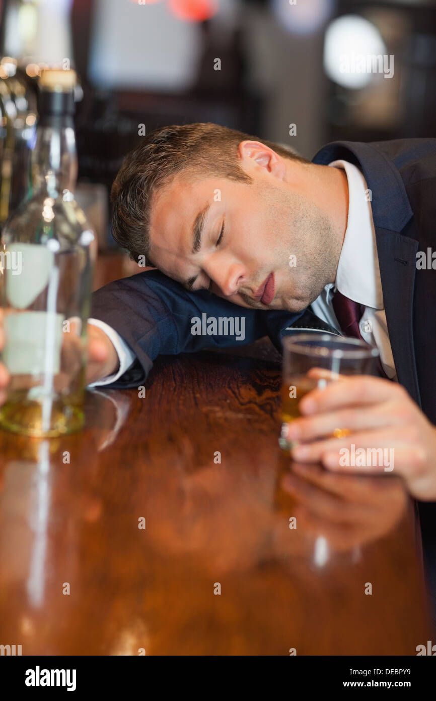Drunk businessman holding whiskey glass lying on a counter Stock Photo