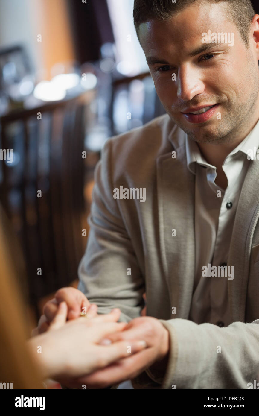 Handsome man putting on ring on his fiances finger Stock Photo
