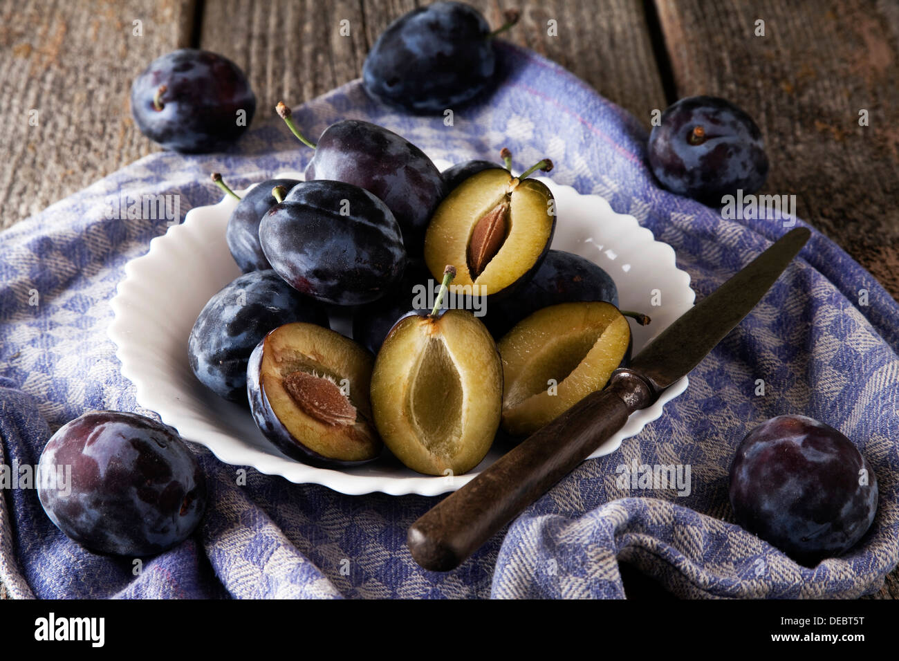 Fresh plums (Prunus domestica) on plate, with a knife and a kitchen towel Stock Photo
