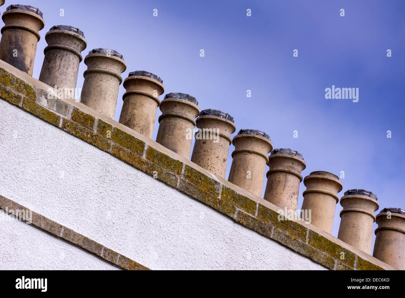 A line of eleven chimney pots on a whitewashed chimney stack stand out against a blue sky. Stock Photo