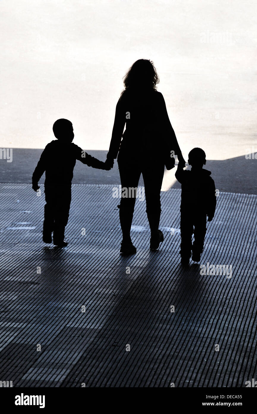 A woman with two children in hand walks out of the dark and into the light Stock Photo