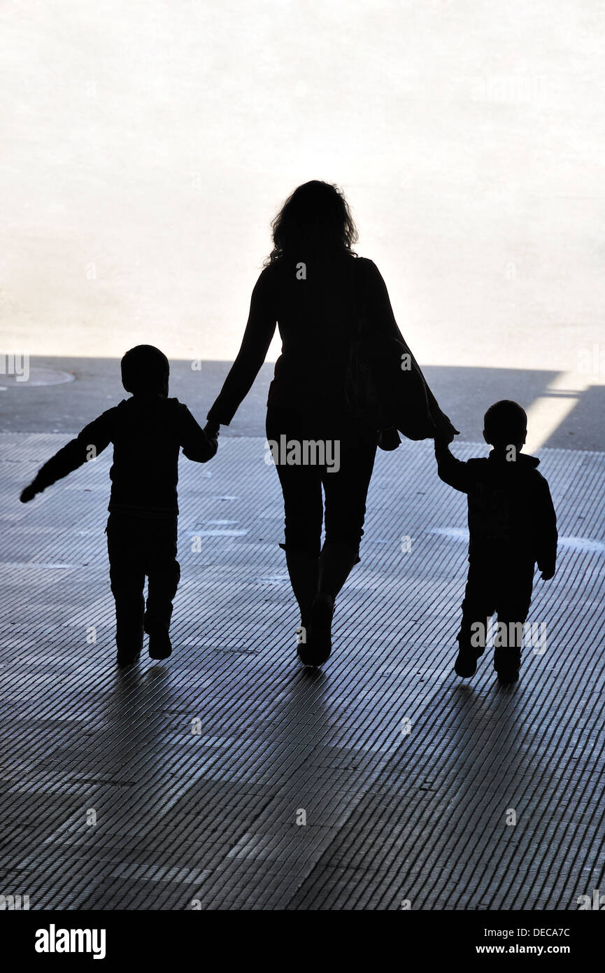 A woman with two children in hand walks out of the dark and into the light Stock Photo