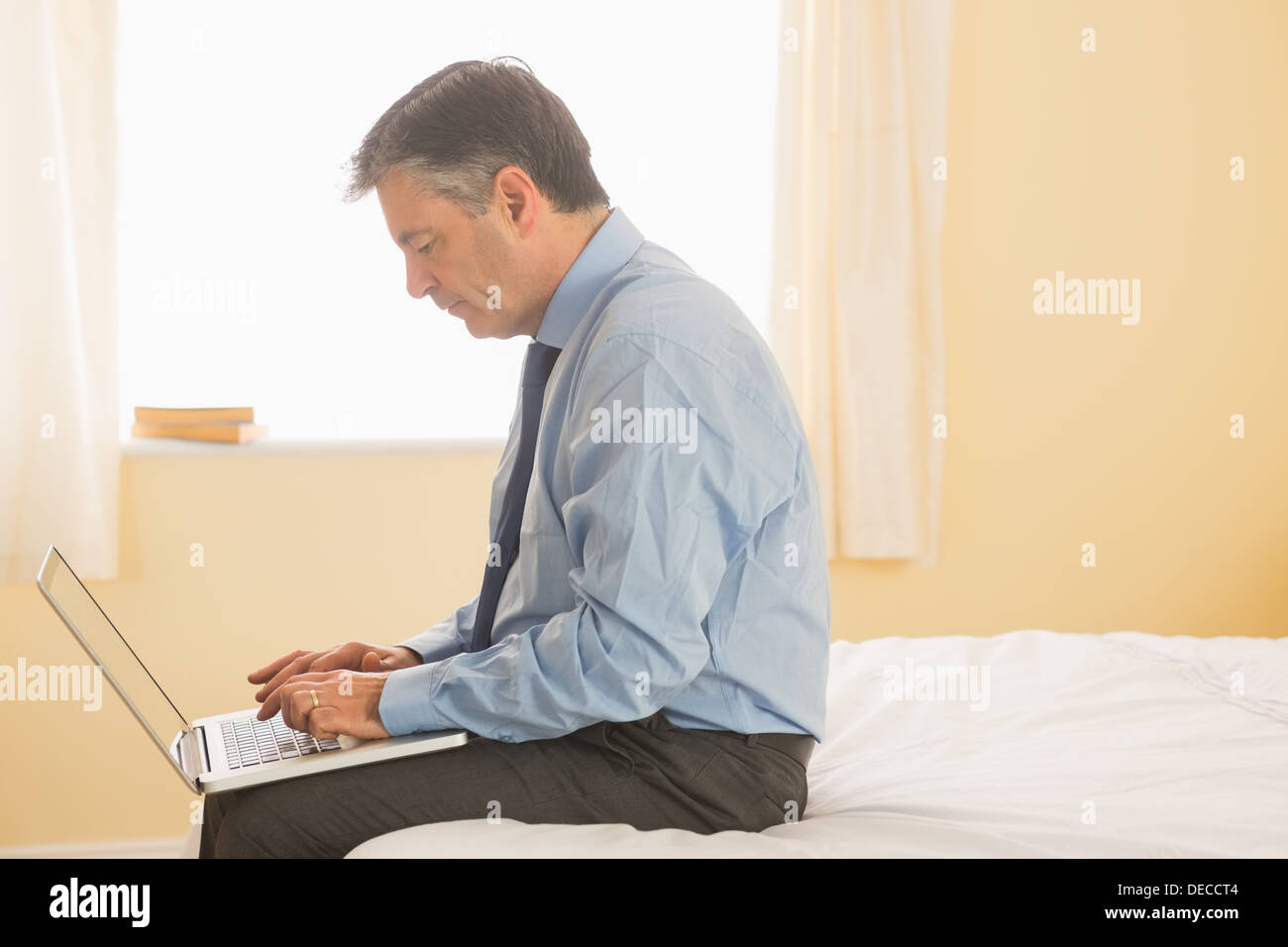Concentrated man using a laptop sitting on bed Stock Photo