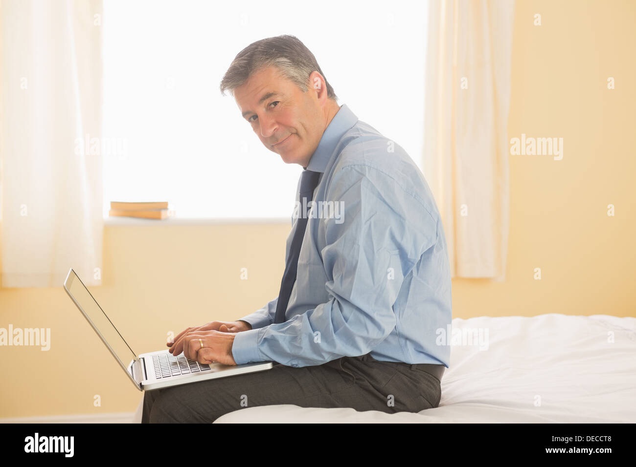 Thoughtful man using a laptop sitting on a bed Stock Photo