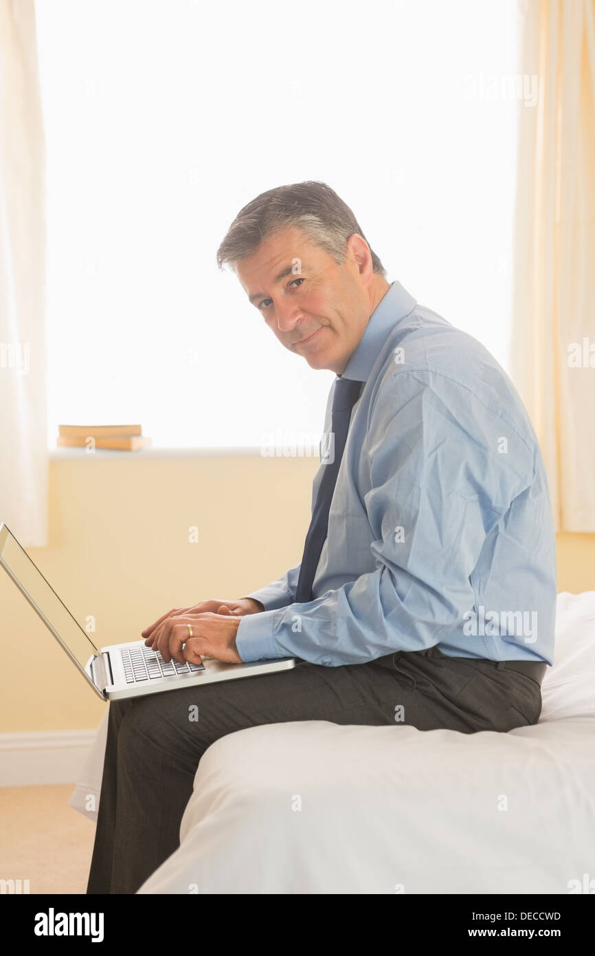 Focused man using a laptop sitting on a bed Stock Photo