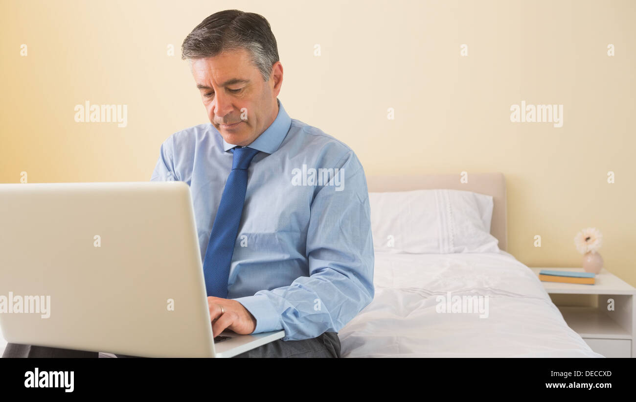 Thoughtfulman using a laptop sitting on a bed Stock Photo