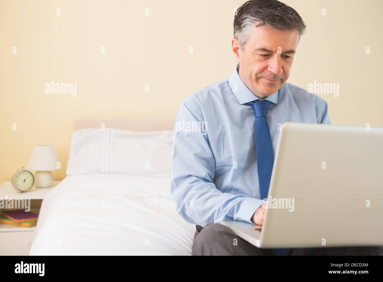 Thoughtful man using a laptop sitting on a bed Stock Photo