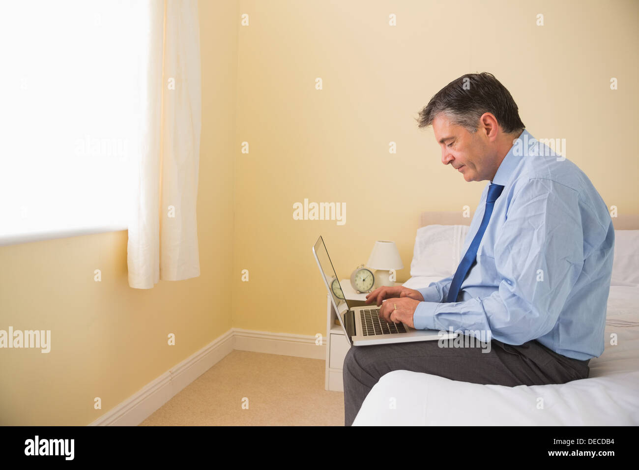 Focused man using a laptop sitting on a bed Stock Photo