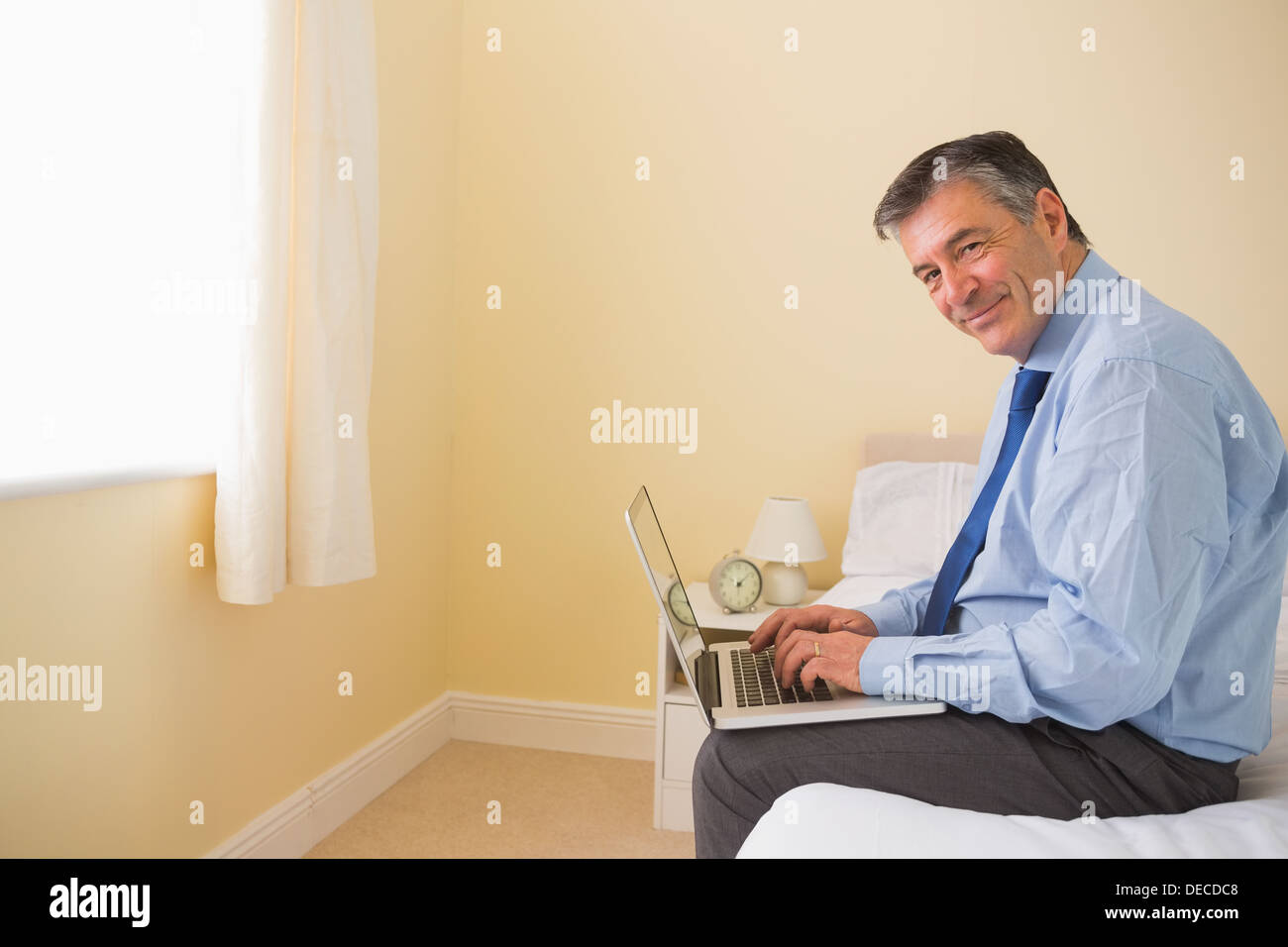Pleased man using a laptop sitting on a bed Stock Photo