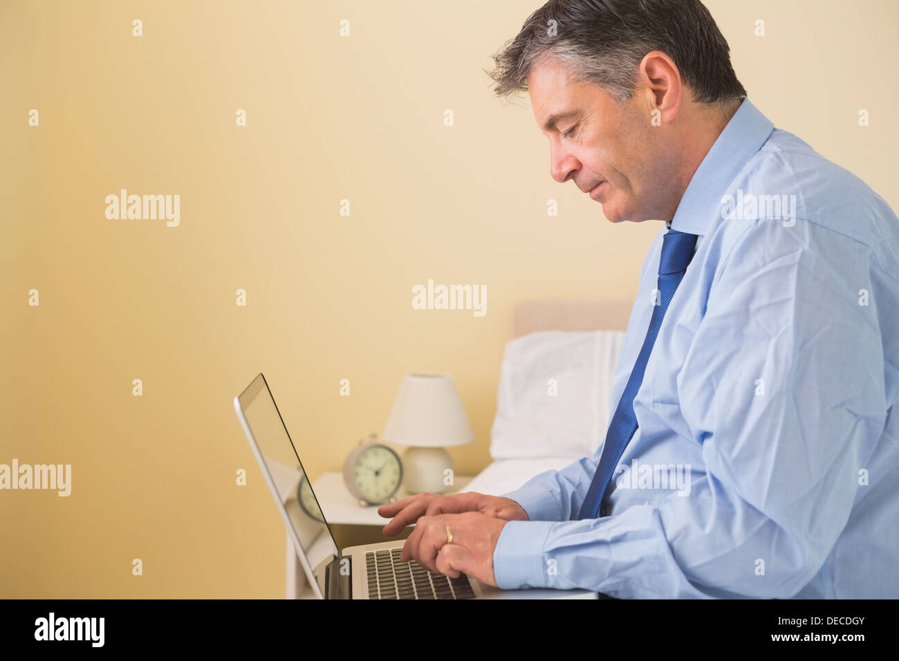 Focused man using a laptop sitting on a bed Stock Photo