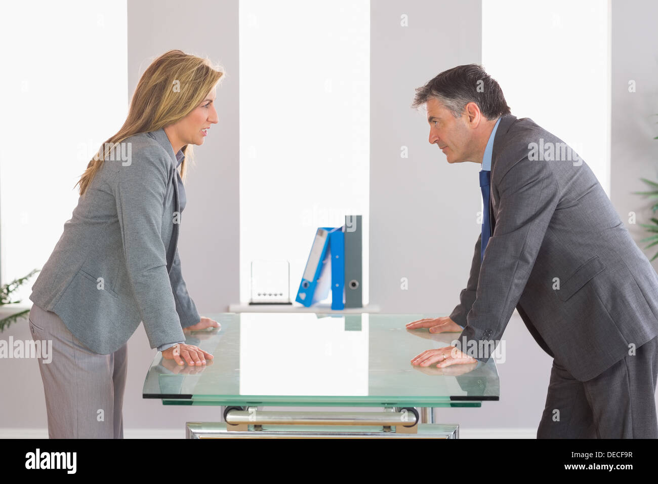 Two irritated businesspeople arguing on each side of a desk Stock Photo