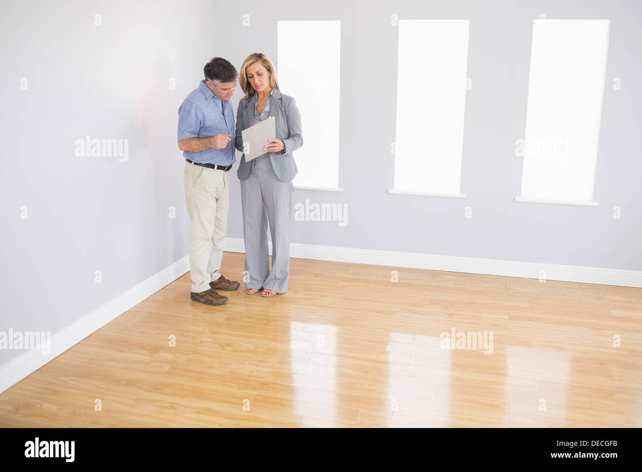 Serious blonde realtor showing a room and some documents to a potential buyer Stock Photo