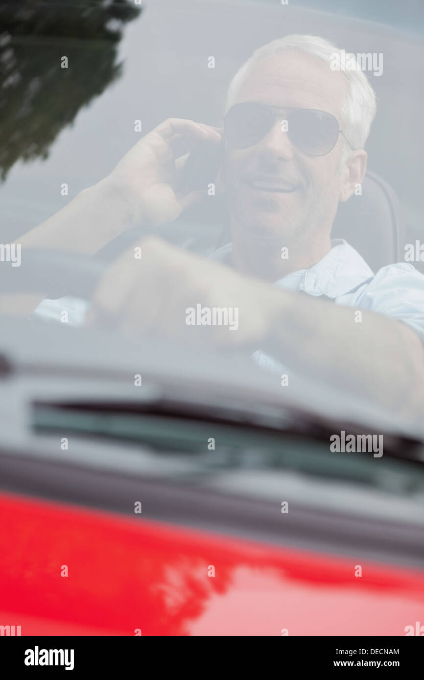 Cheerful handsome man in red convertible having phone call Stock Photo