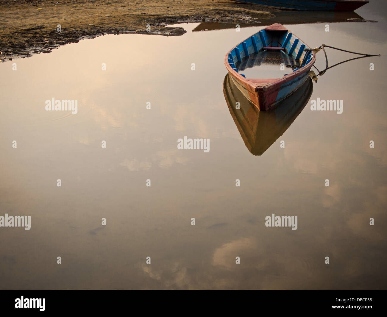 A wooden rowing boat marooned, anchored, floating on the still waters of a lake. Stock Photo
