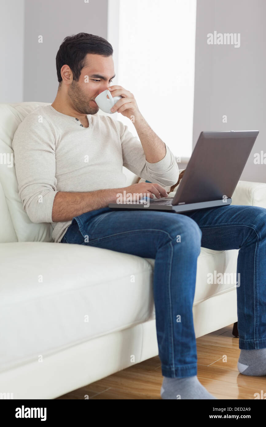 Relaxed attractive man drinking coffee while working on his laptop Stock Photo