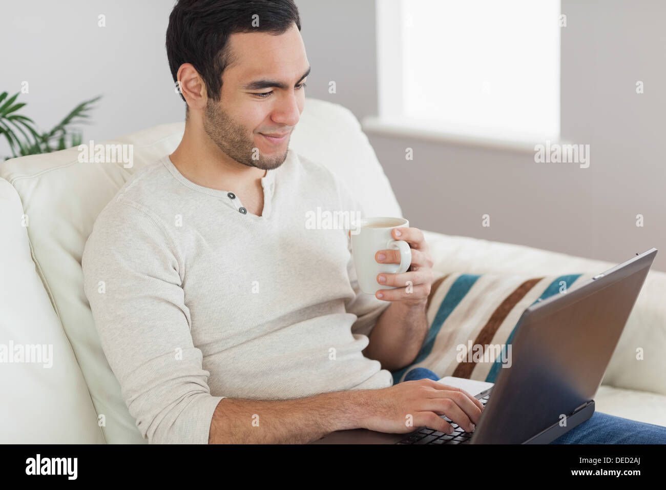 Calm attractive man drinking coffee while working on his laptop Stock Photo