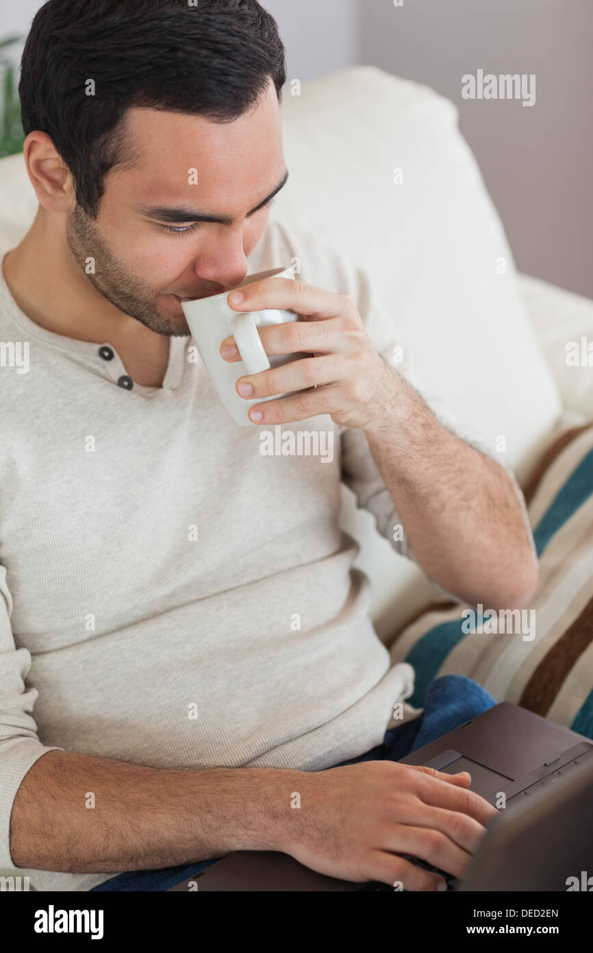 Peaceful attractive man drinking coffee while using his laptop Stock Photo