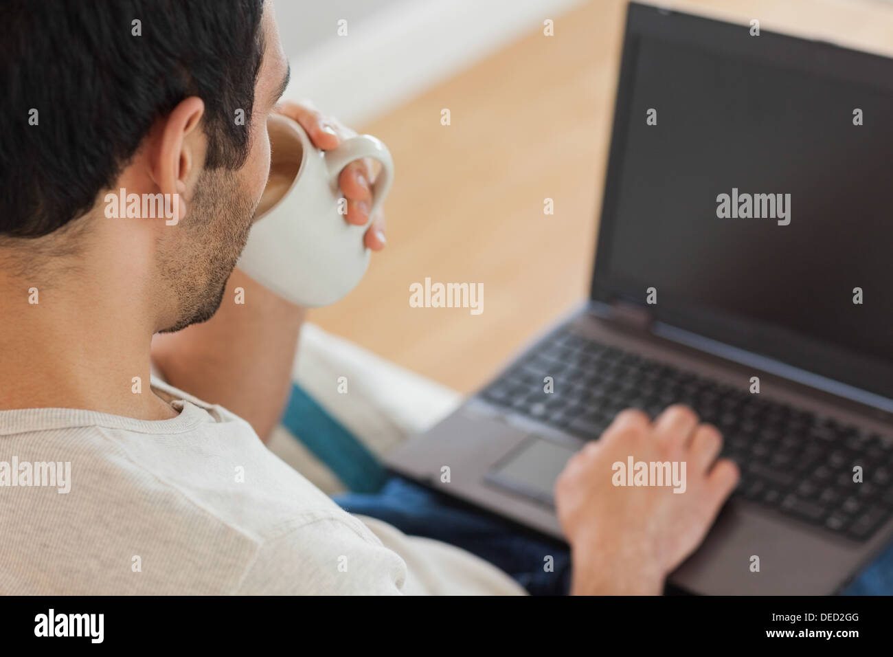 Handsome brown haired man drinking coffee while using his laptop Stock Photo