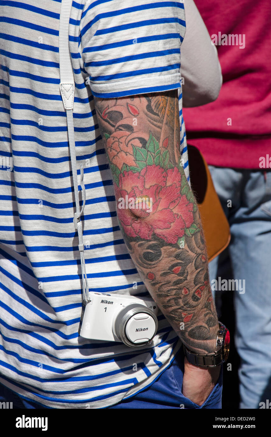 Man with a tattooed arm and a Nikon camera on the High Street in Edinburgh. Stock Photo