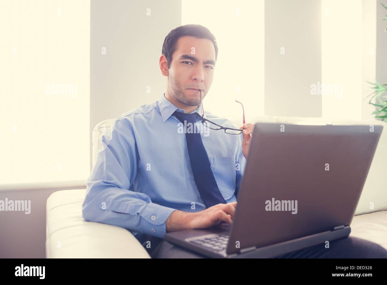Nervous man biting his eyeglasses and using a laptop Stock Photo