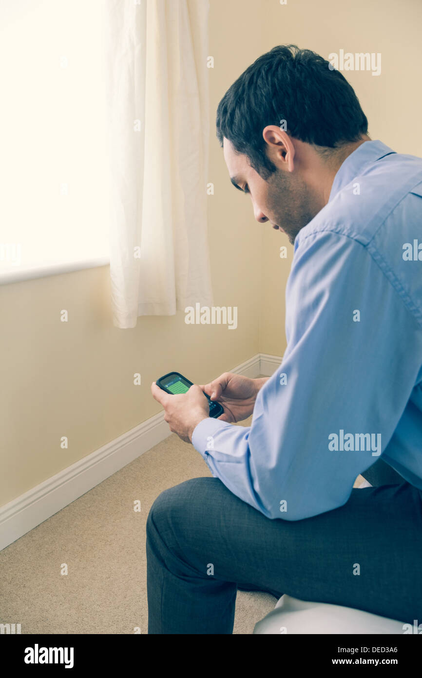 Man using a mobile phone sitting on a bed Stock Photo