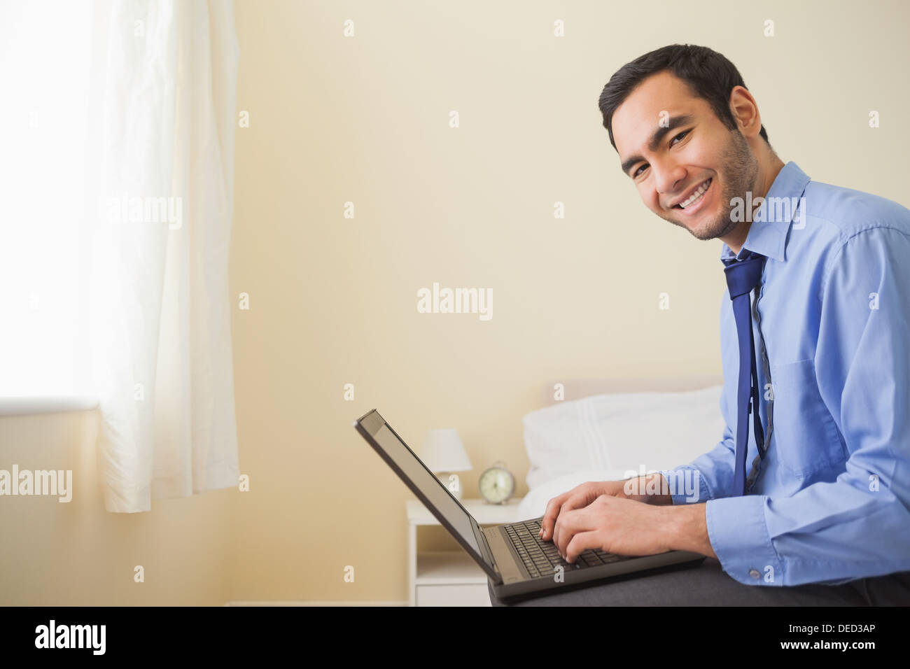 Smiling man using a laptop sitting on bed Stock Photo