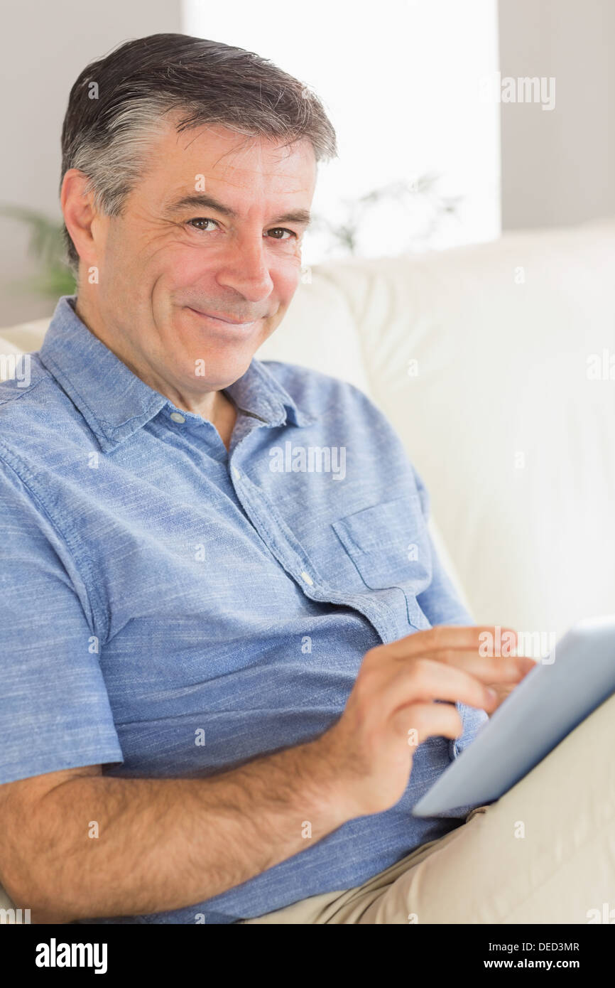 Smiling man sitting on a sofa using a tablet pc Stock Photo