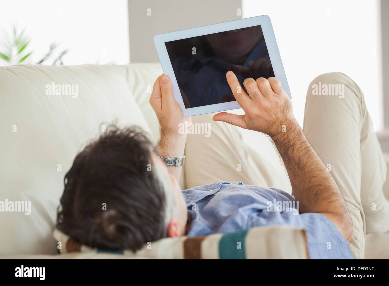 Man laying on sofa using a tablet pc Stock Photo