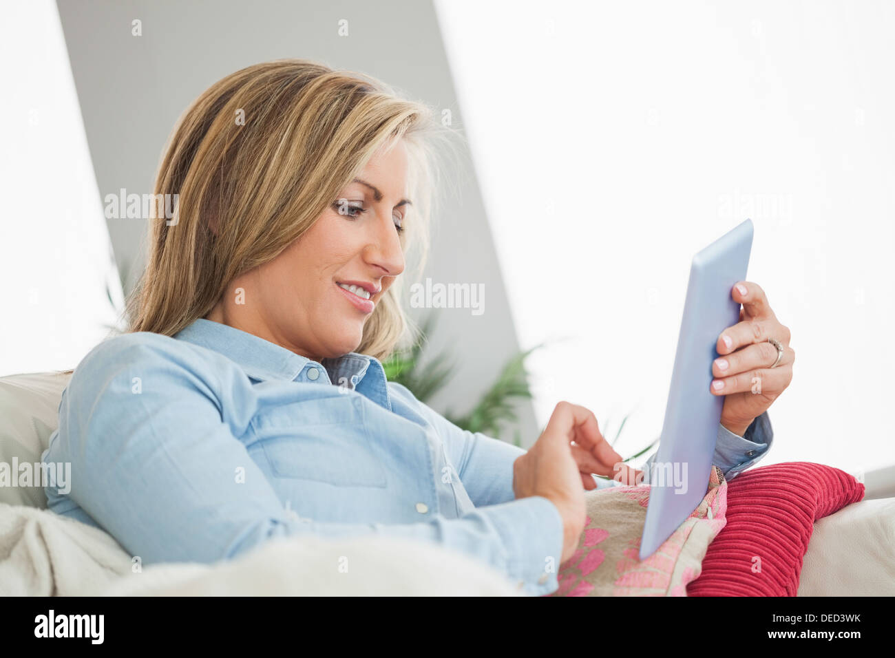 Smiling woman lying on sofa using a tablet pc Stock Photo
