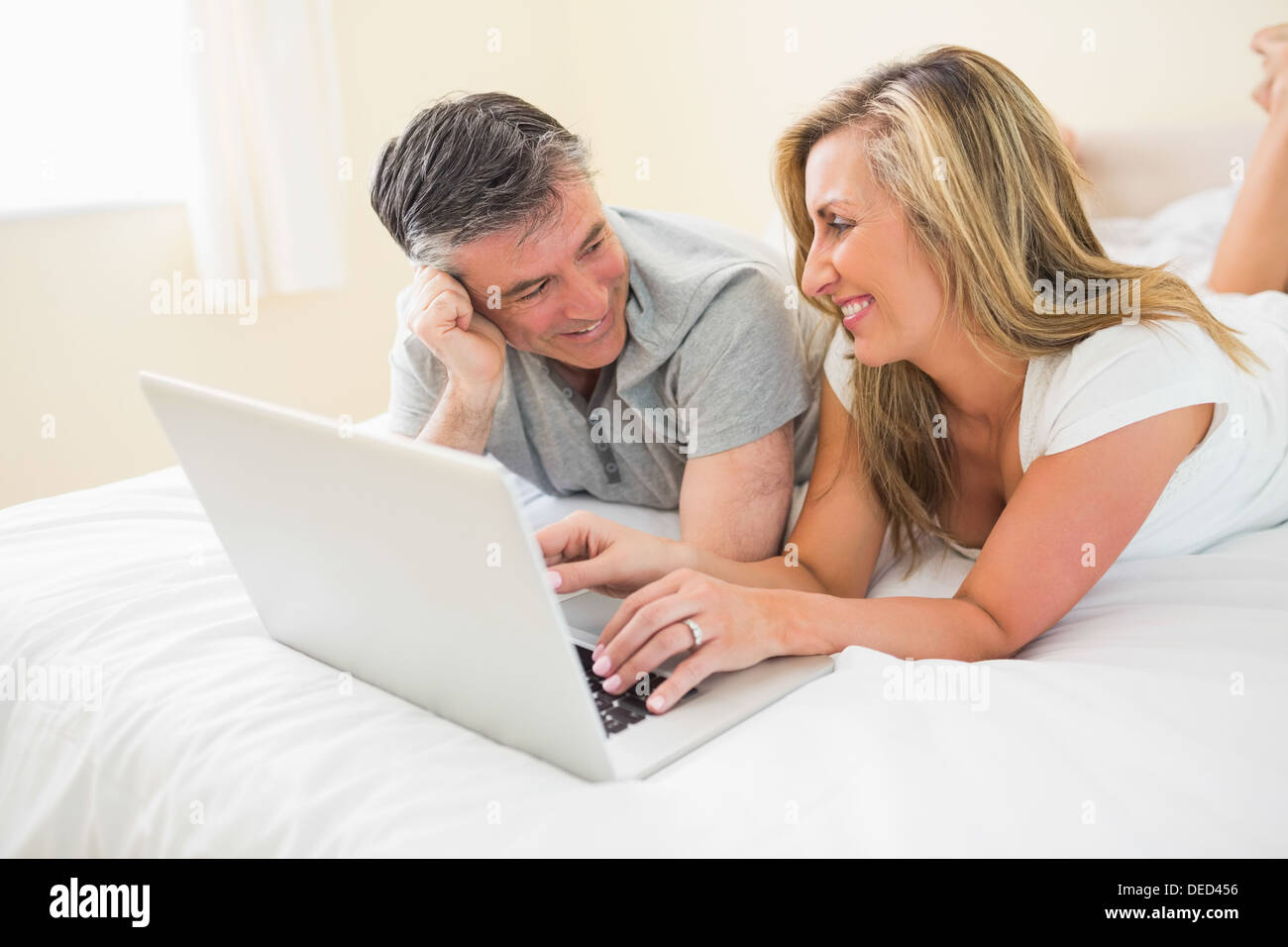 Laughing couple lying on bed using a laptop Stock Photo