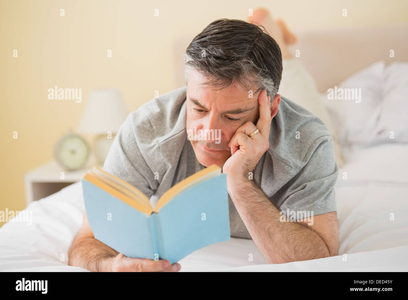 Concentrated man reading a book on his bed Stock Photo