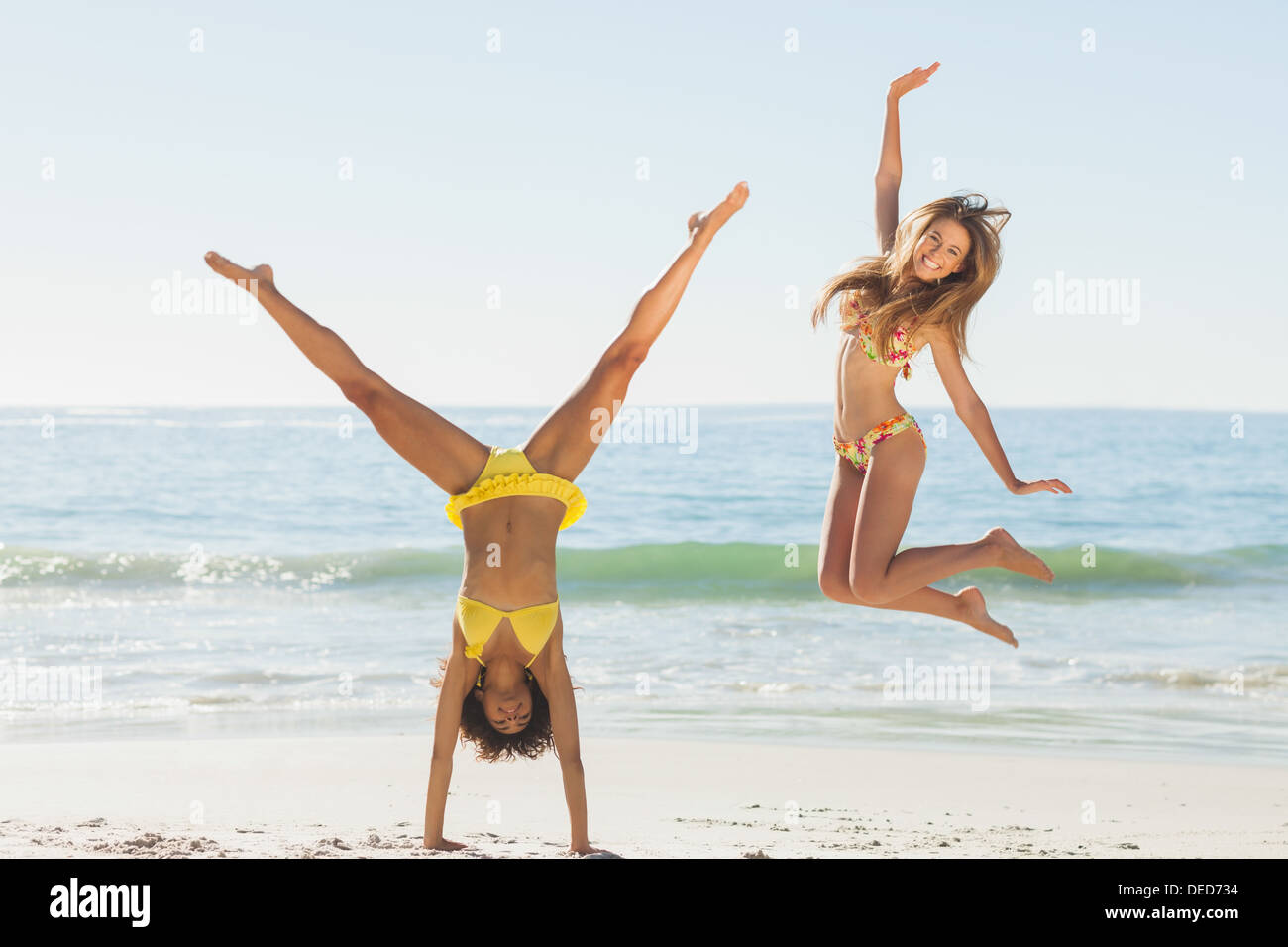 Friends in bikinis jumping and doing handstand Stock Photo