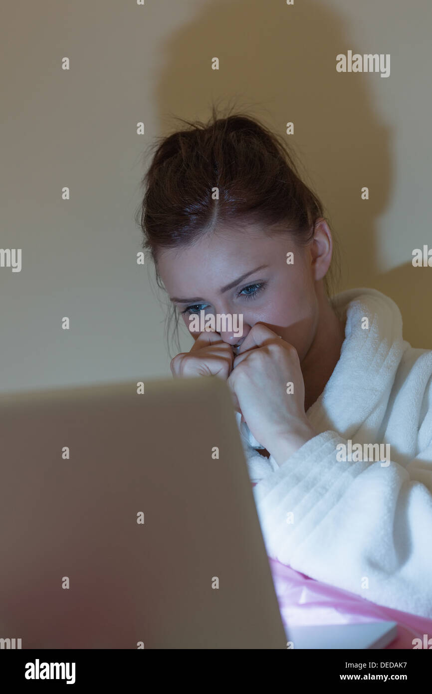 Pretty teen wearing dressing gown watching her laptop in the dark Stock Photo
