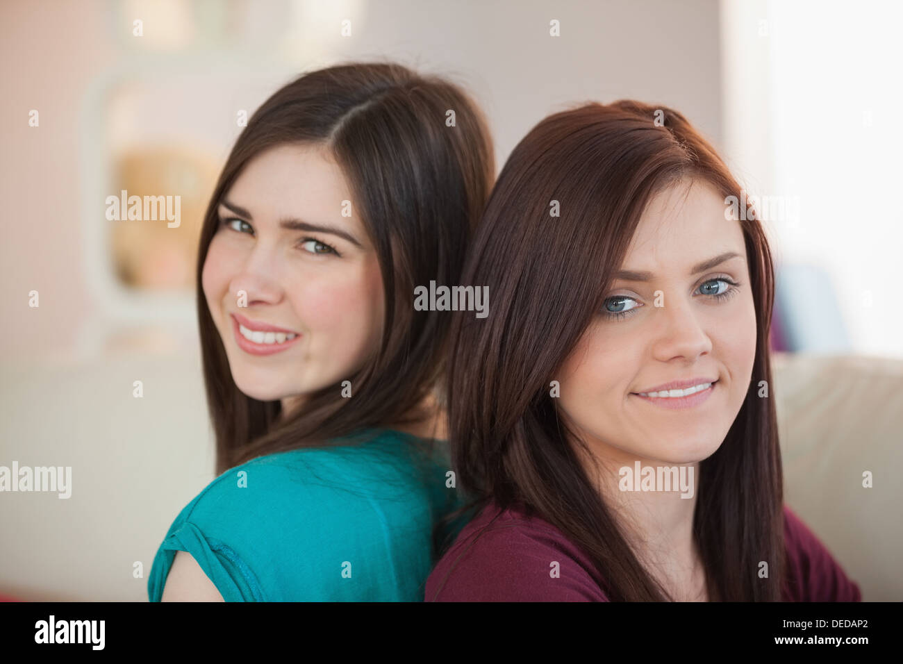 Two happy friends sitting back-to-back on the sofa Stock Photo