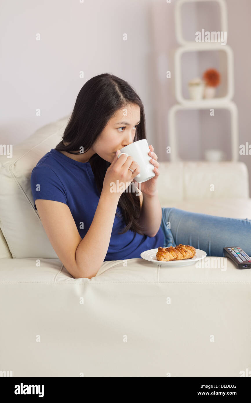 Woman sitting on the sofa drinking coffee with a pastry Stock Photo