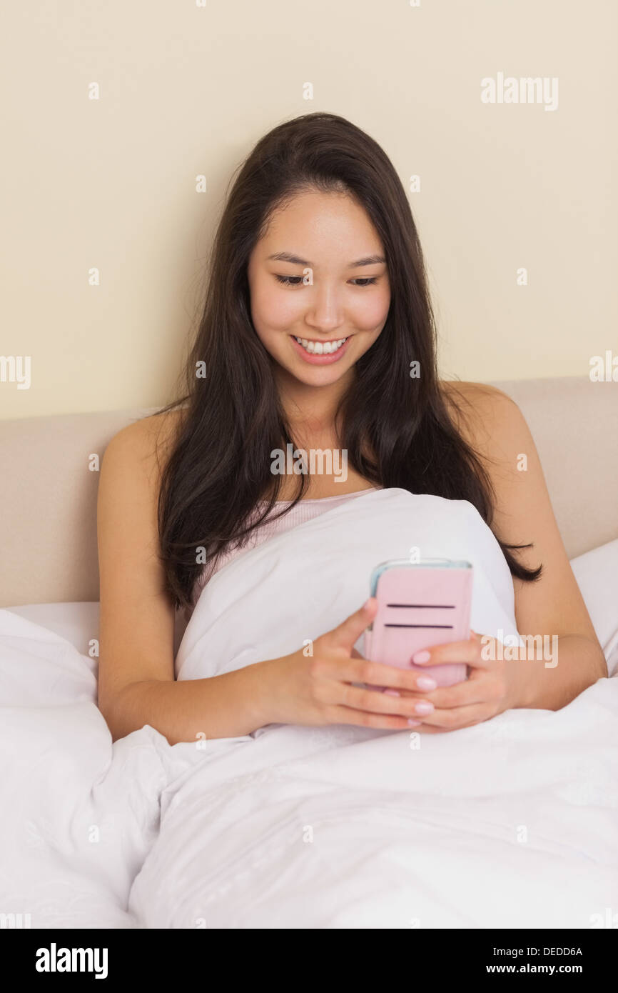 Young asian woman sitting in bed using smartphone Stock Photo - Alamy