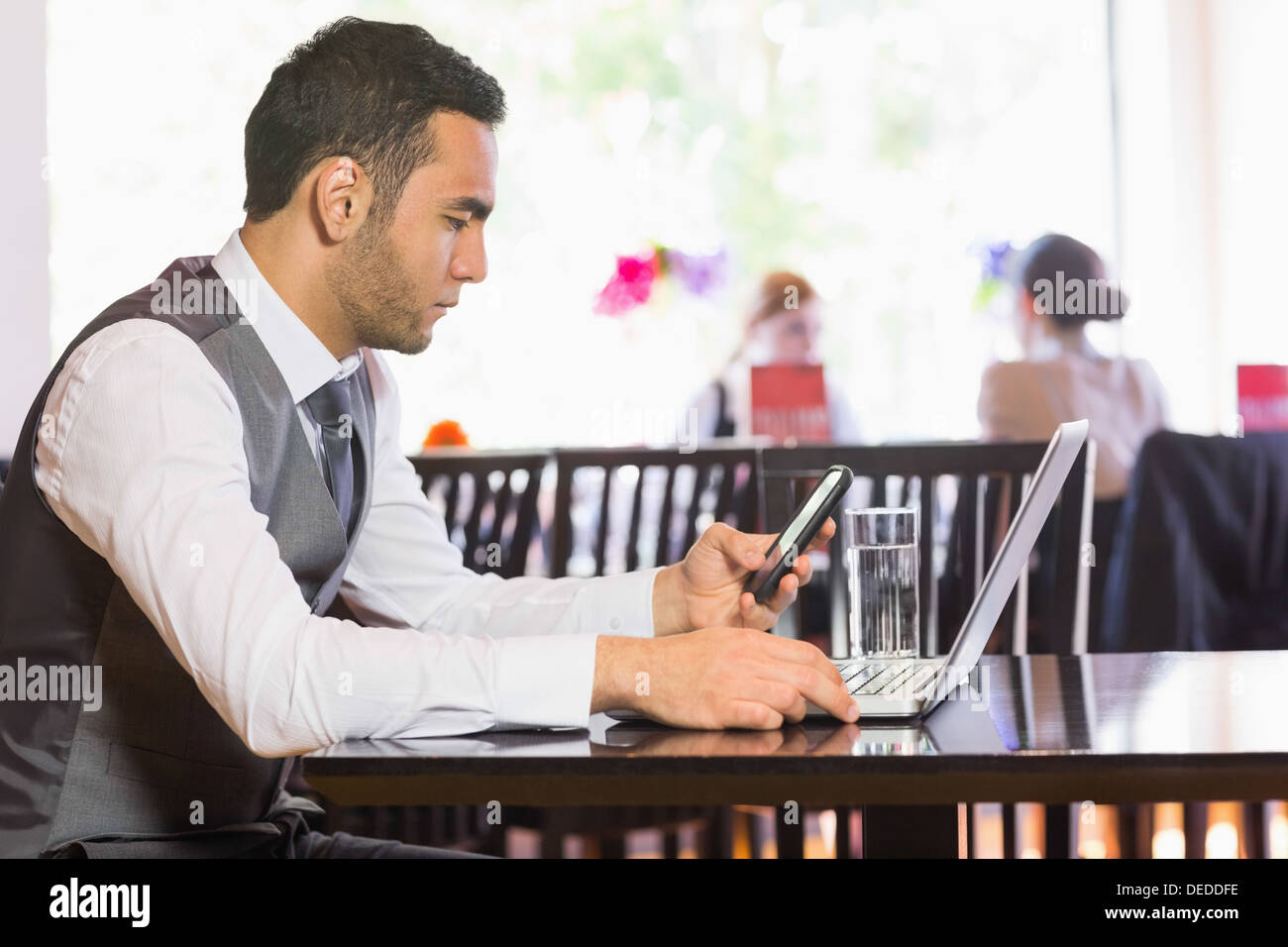 Serious businessman using phone while working on laptop Stock Photo