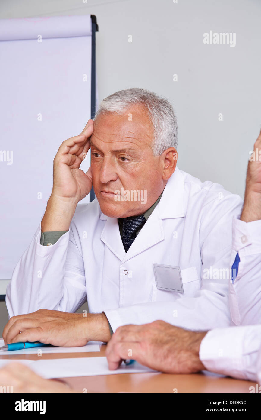 Pensive senior doctor thinking in a team meeting Stock Photo - Alamy