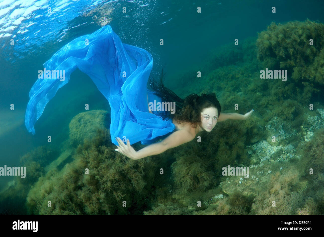 A young woman with long hair in a blue dress dives underwater in Black Sea Stock Photo