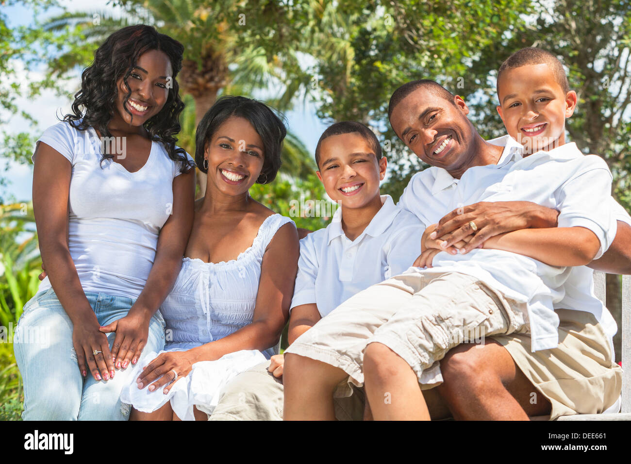 A happy black African American family of two parents and three children, two boys one girl, sitting together outside. Stock Photo