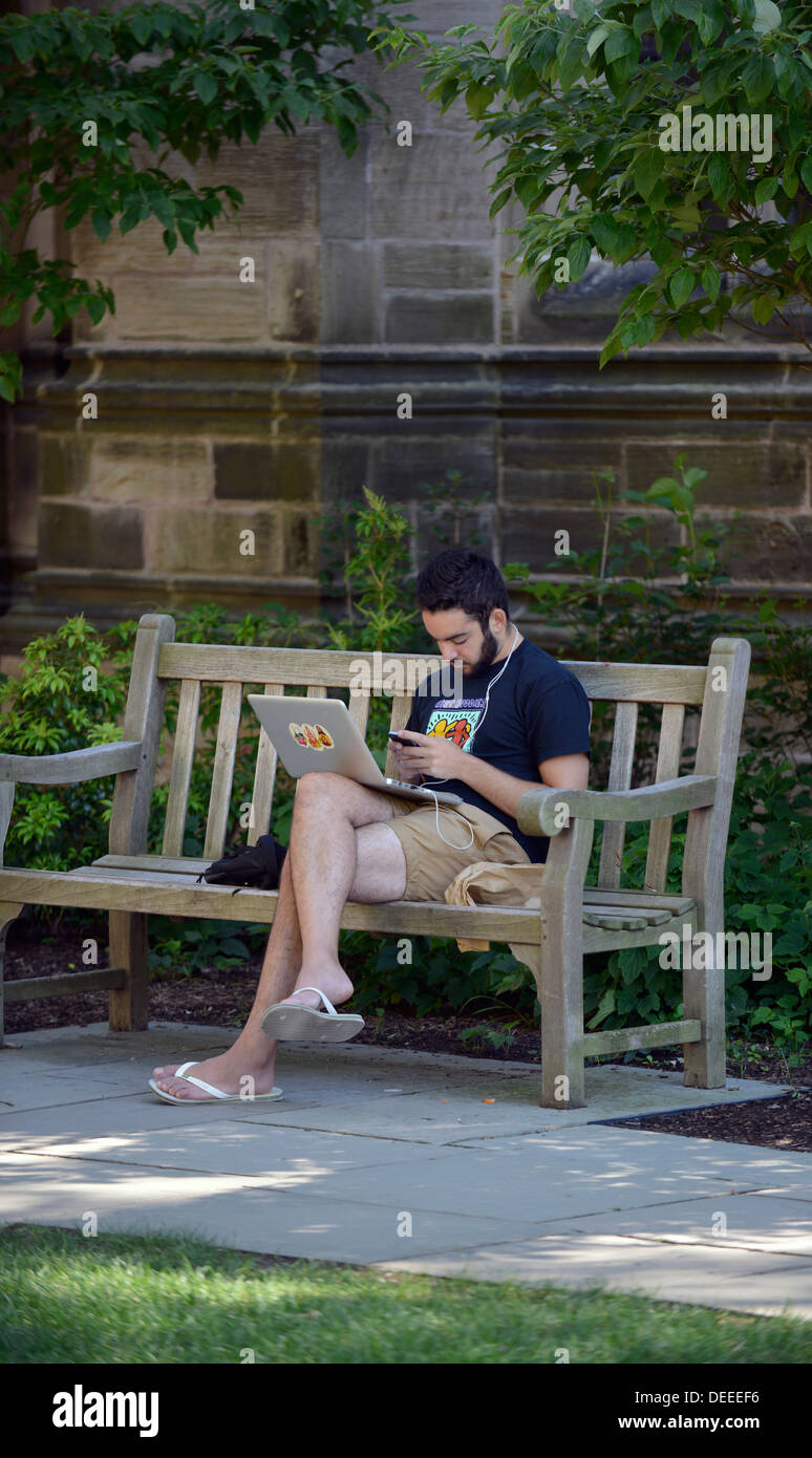 Yale University student listens to music on his smartphone while using his laptop computer. Stock Photo