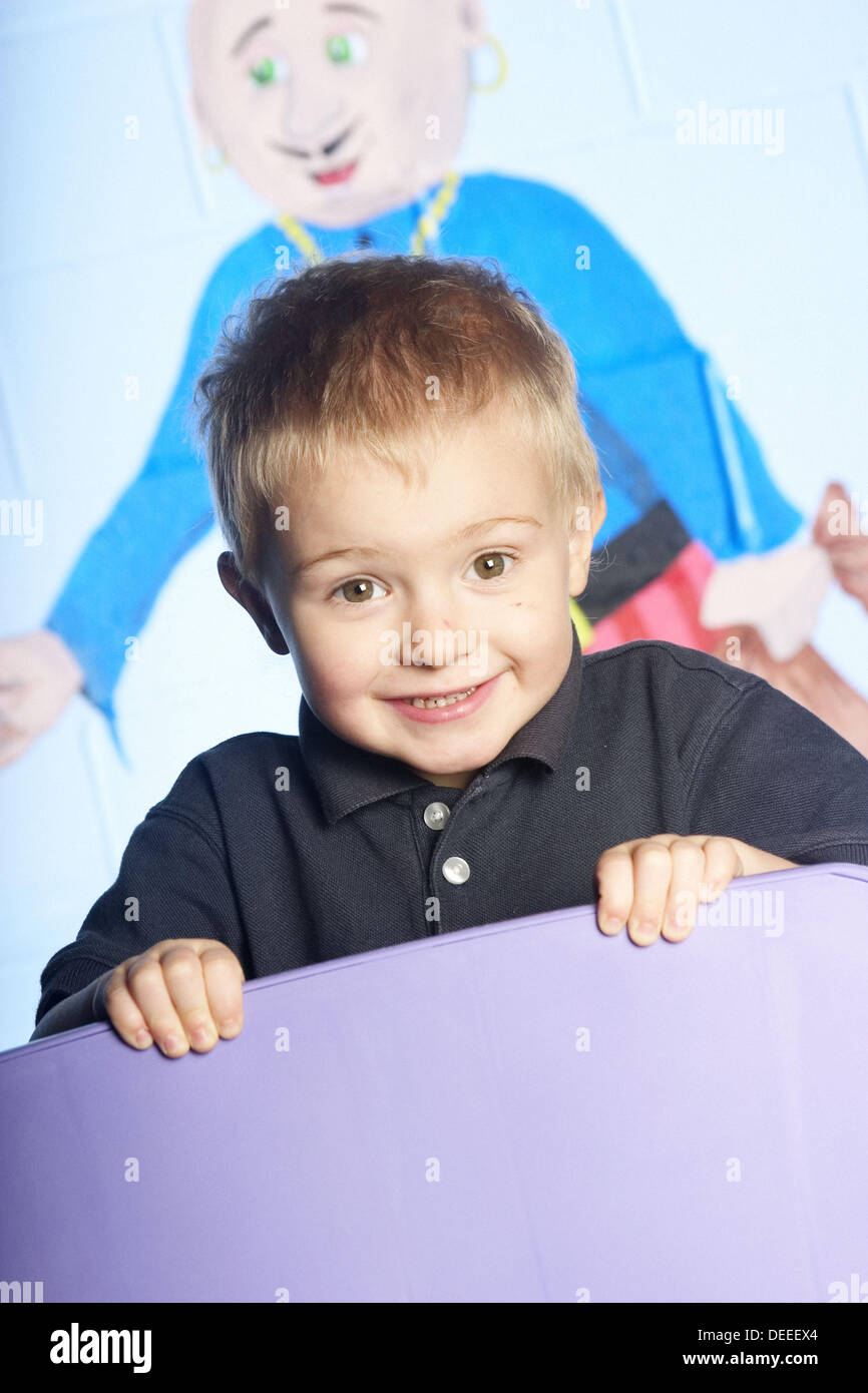3 year old boy leaning over the back of a chair, looking into camera