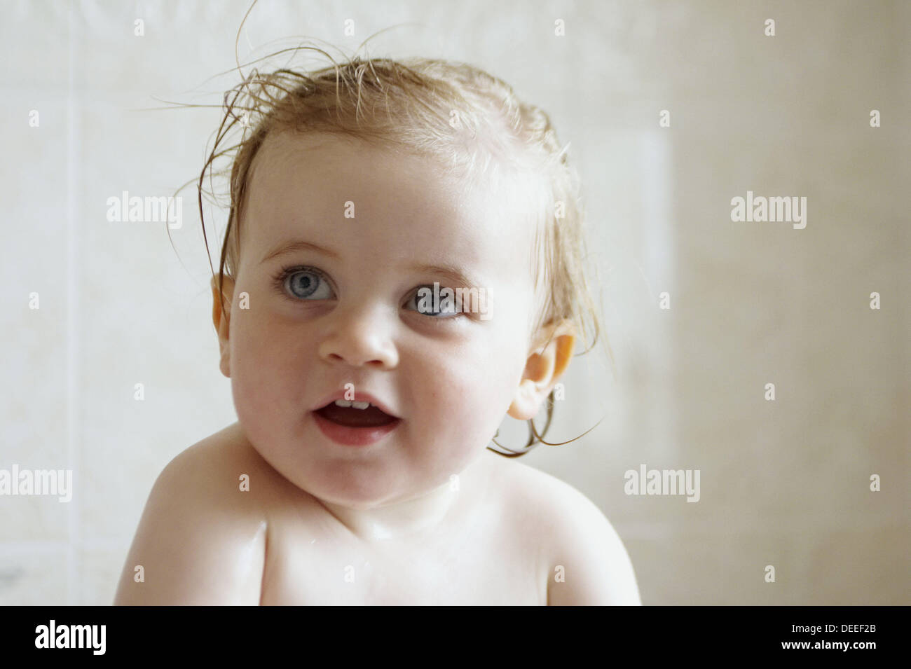 18 month old baby girl, sitting in the bath, smiling off camera Stock