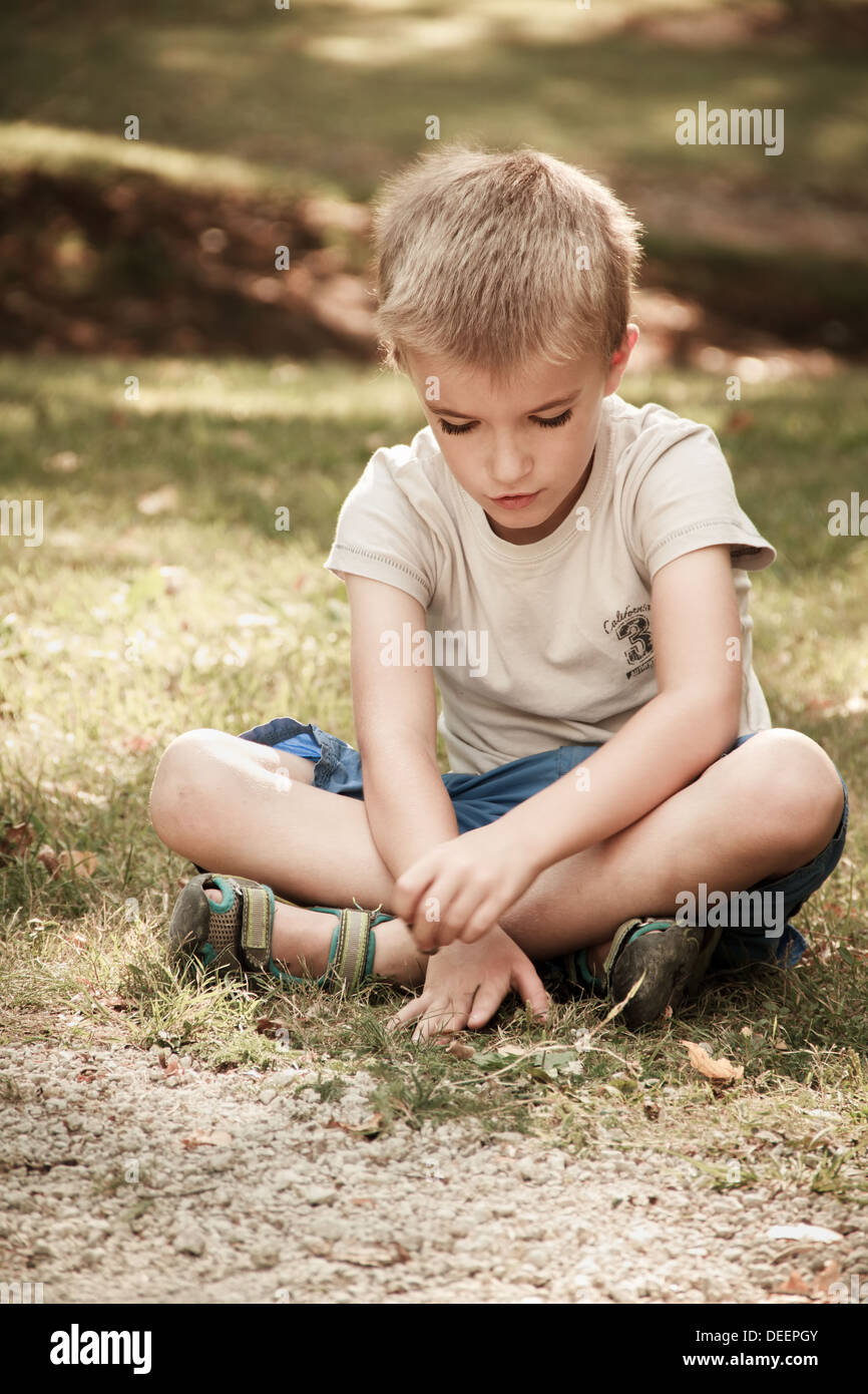 Boy (7 years) sitting on grass Stock Photo - Alamy