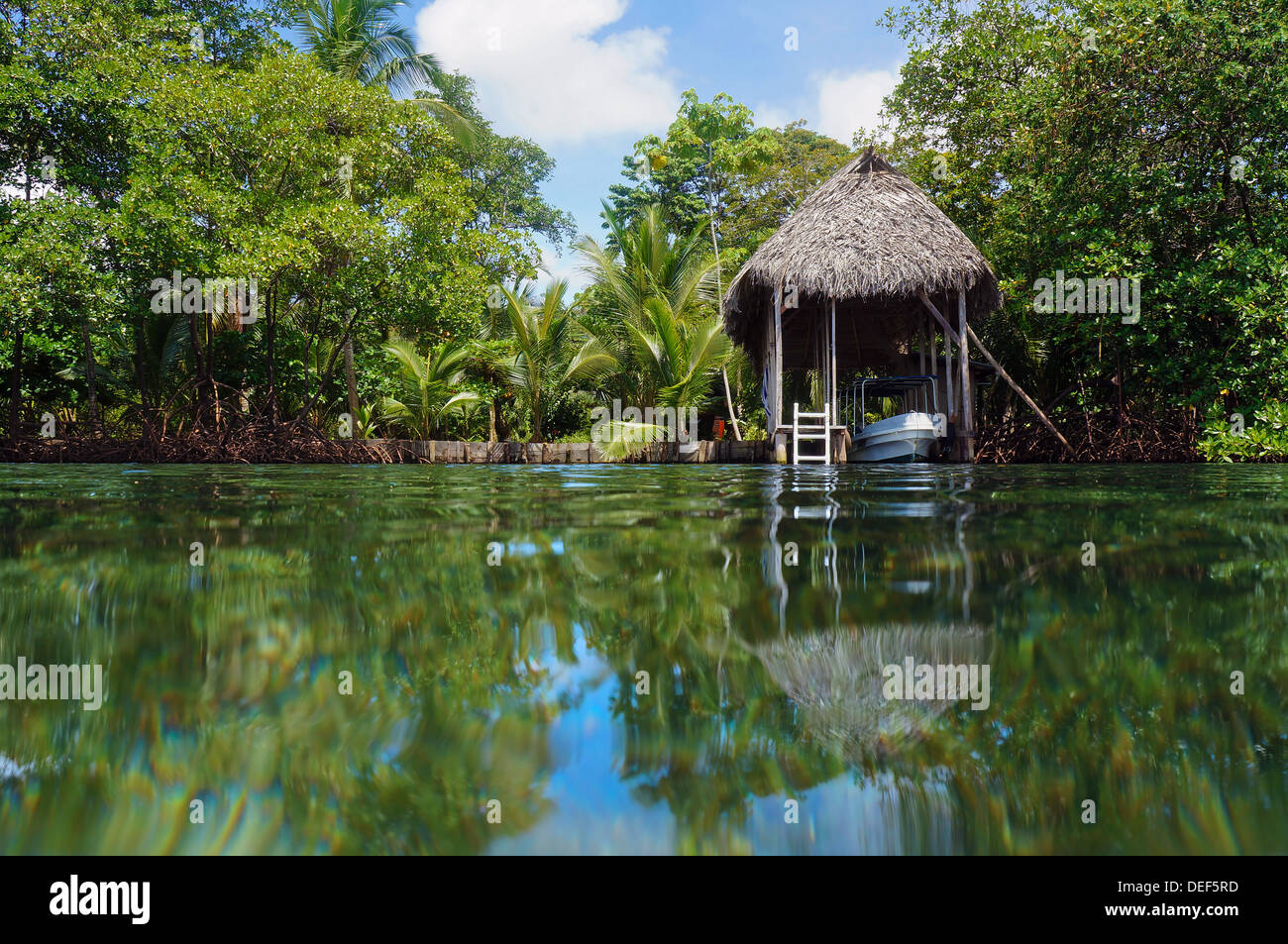 Boathouse with palm roof and lush tropical vegetation reflected on water surface, Bocas del Toro, Caribbean sea, Panama Stock Photo
