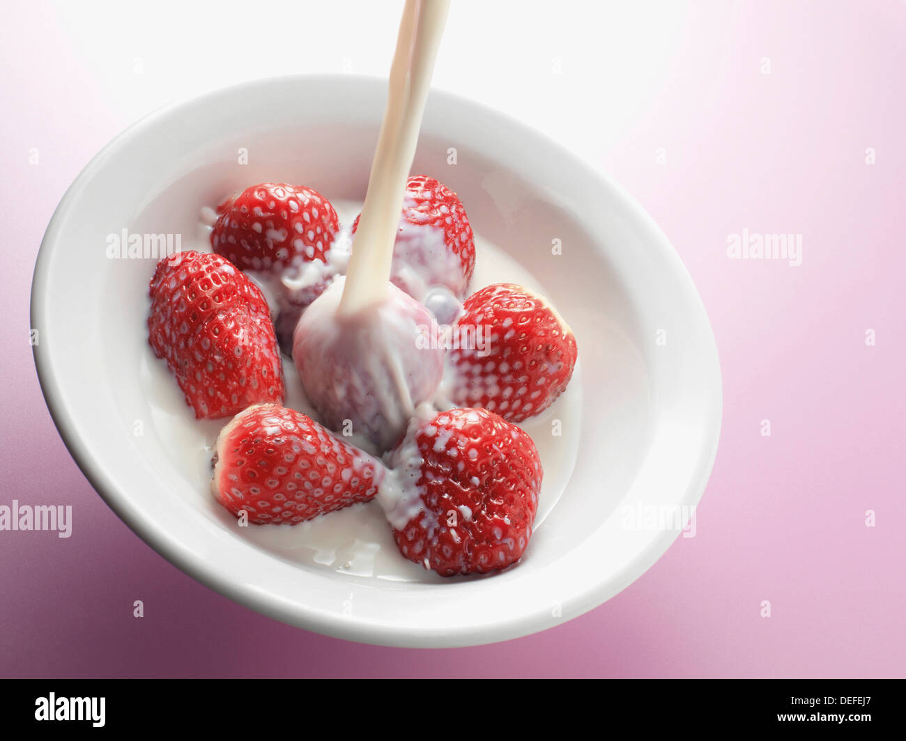 Fresh milk being poured onto a bowl of strawberries Stock Photo